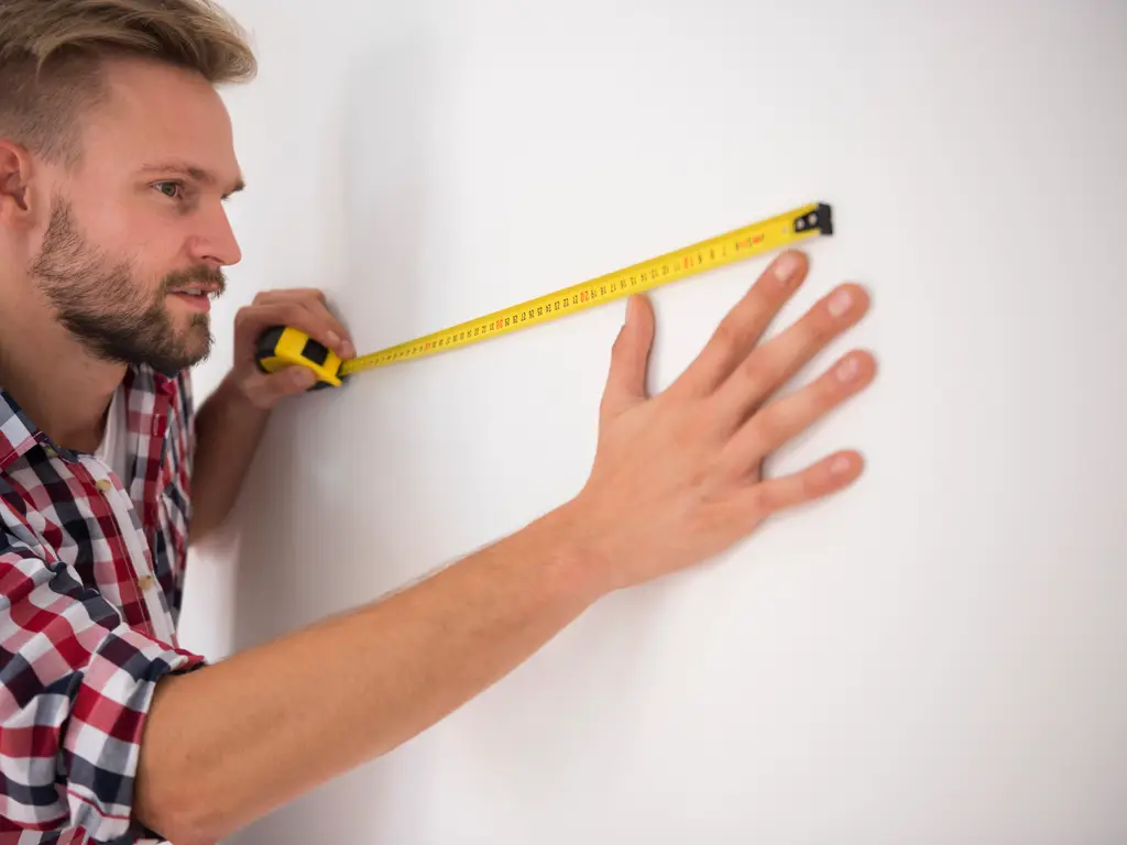A man measuring along a wall with a yellow tape measure