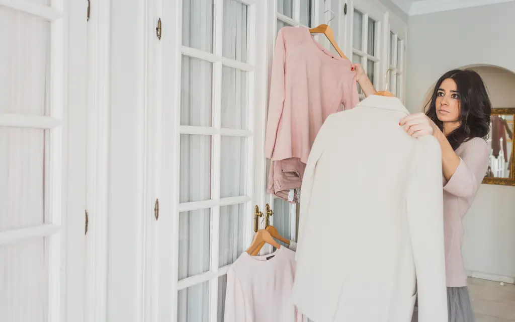 A woman comparing two garments on hangers, deciding between them (illustrative photo)