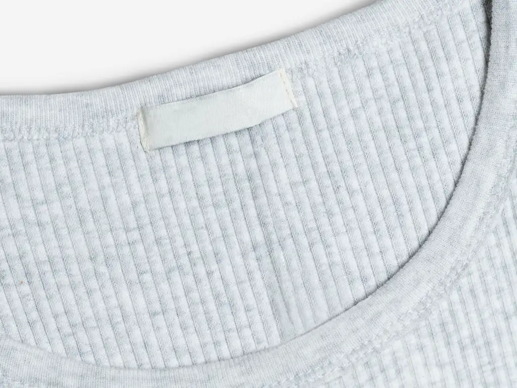 Close-up of the neckline of a ribbed light grey T-shirt with a small blank sewn-in label