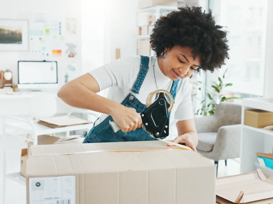 An owner sealing a shipping box with tape at the packing table (illustrative photo)
