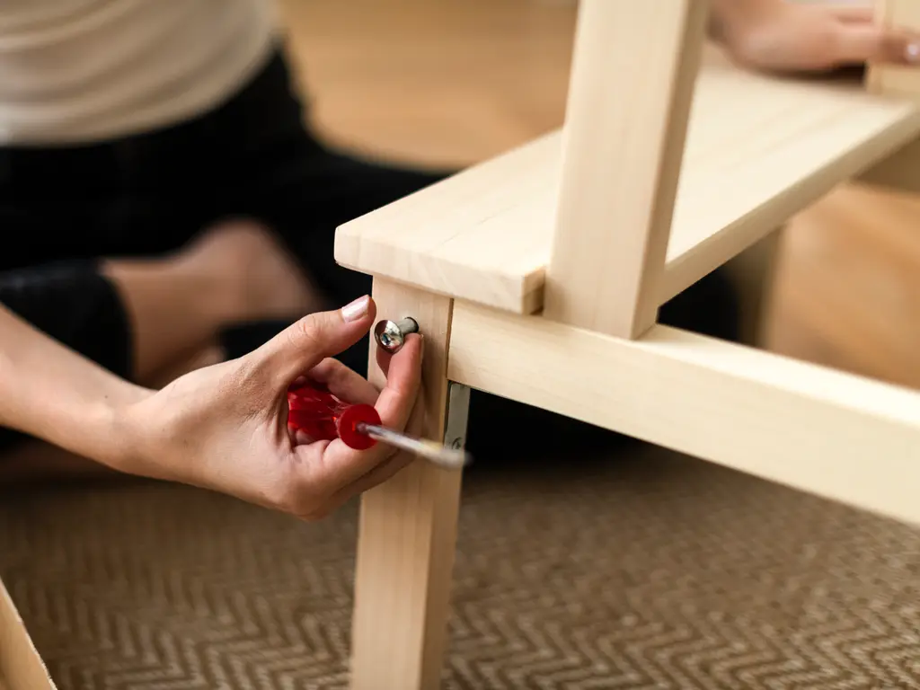 Hands tightening a screw into a wooden chair frame, with an open carton on the floor